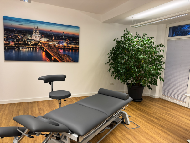 Behandlungsraum Behandlungsraum mit einer Liege, einem Stuhl und einem großen Fenster mit Stadtansicht.